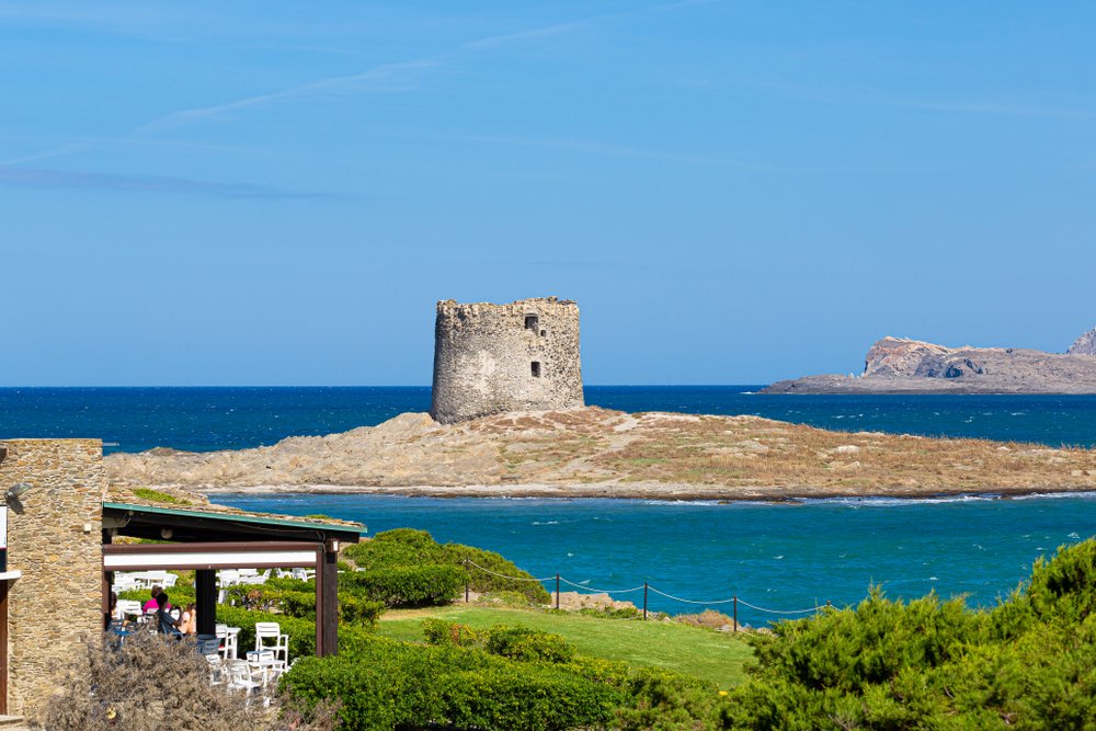 the view of the islands off the coast of stintino, one which has the ruins of an old tower, and another one off further in the distance in sparkling blue sea.