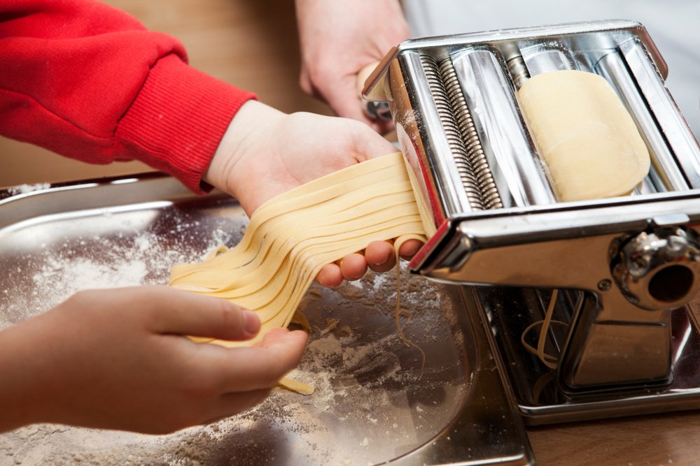Person hand-making egg pasta with a pasta machine
