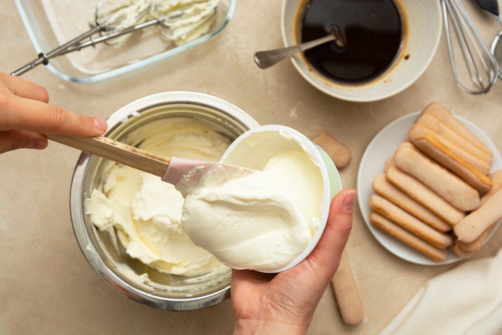 Person in a Sicily cooking class creating tiramisu with whipped mascarpone, lady finger cookies and espresso or cocoa powder