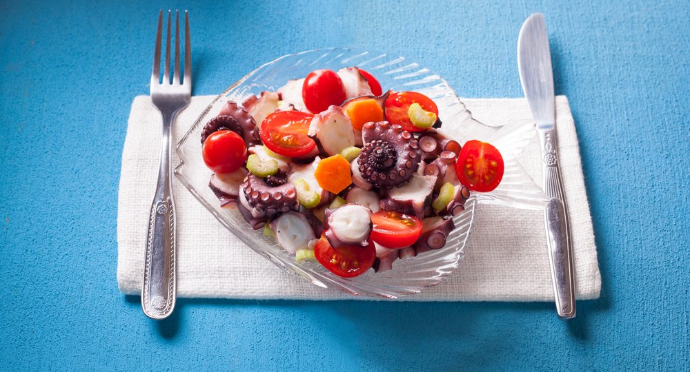 Cold salad with octopus, tomatoes, stem celery, carrots, olive oil, lemon juice and black pepper, a typical dish of Sicily, Italy; on a blue background