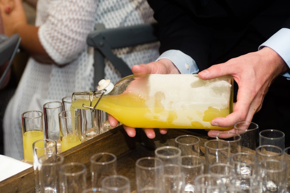 Man pouring homemade limoncello out of a bottle into small cups