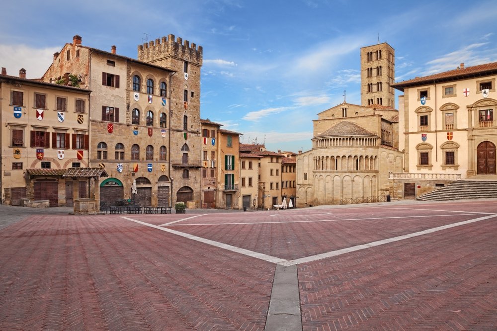 the city of arezzo with golden colored buildings on a sunny day with no one out in the piazza which is empty and clear