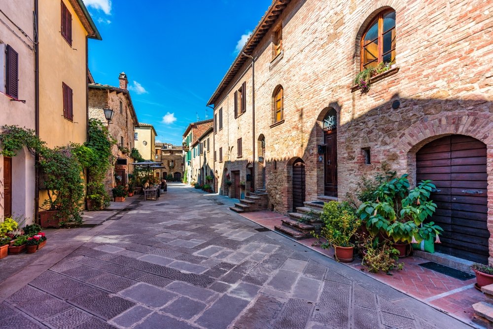 Cozy narrow street decorated with colorful flowers in the charming town of Pienza in Tuscany, a small and historic village.