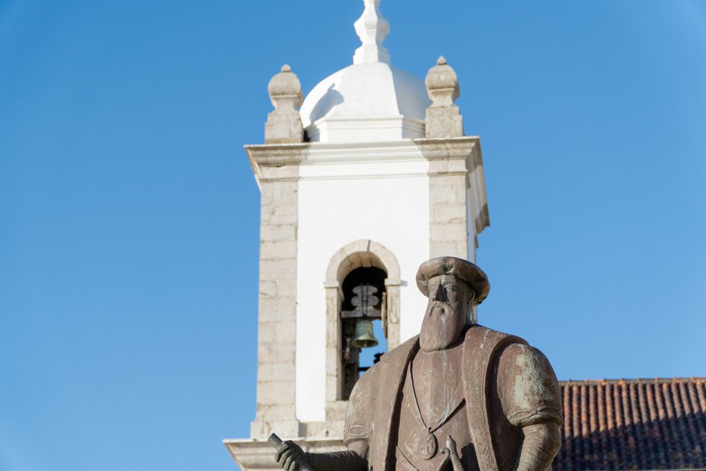 Vasco da Gama Statue and Sines church bell house close up with a sunny sky as the backdrop, not a cloud in sight.