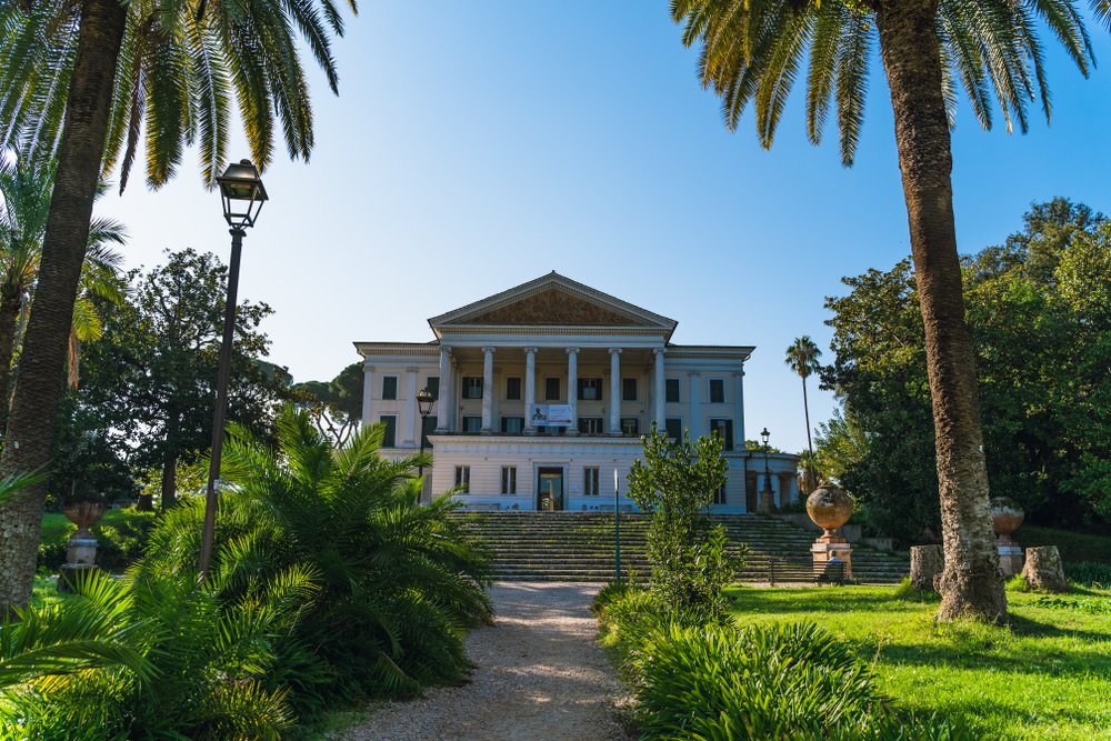 Museum of Villa Torlonia in a park, Rome, Italy: a beautiful old historic white building in a grassy field with steps leading up to the museum.