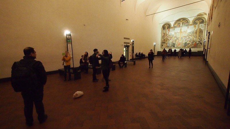 the mostly-empty room that houses the last supper in milan with people looking at the painting