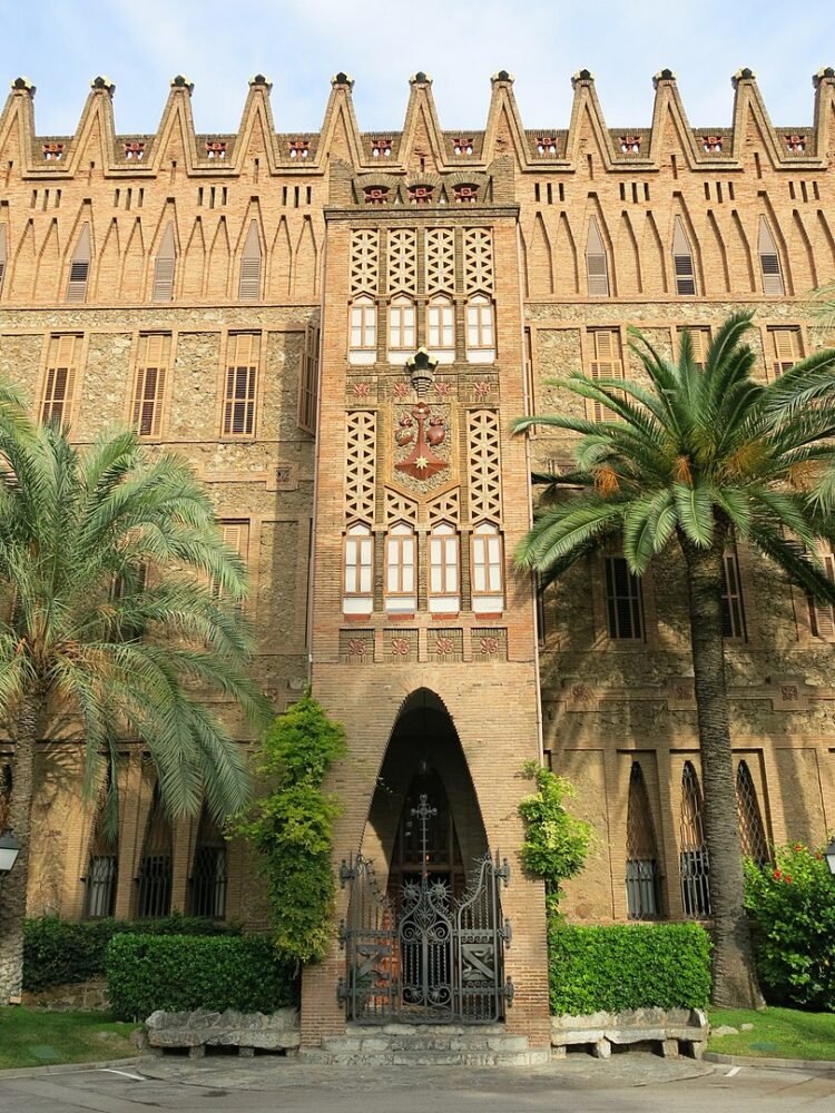 ornate facade of the college that Gaudi designed in barcelona with moorish detailing and palm trees