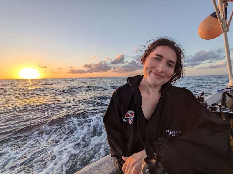 Allison Green with a happy smile on her face looking at the camera as the sun sets as she goes home on the dive boat in Cozumel
