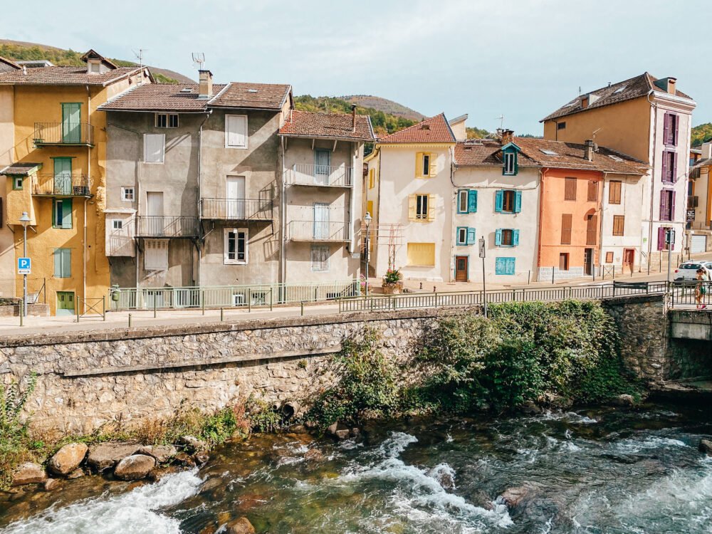 houses alongside a rushing river with colorful building colors and painted shutters in a charming french village