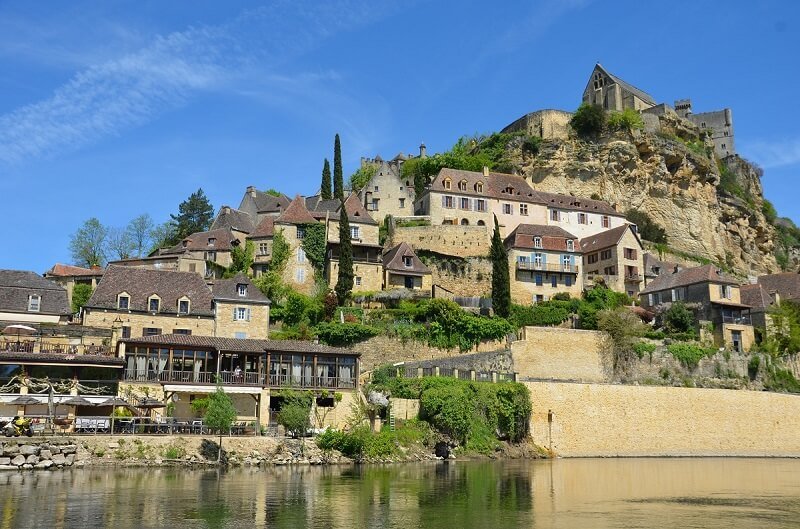 the town of beynac situated on a river with beautiful rivers of the dordogne region, and medieval buildings along a hilltop town