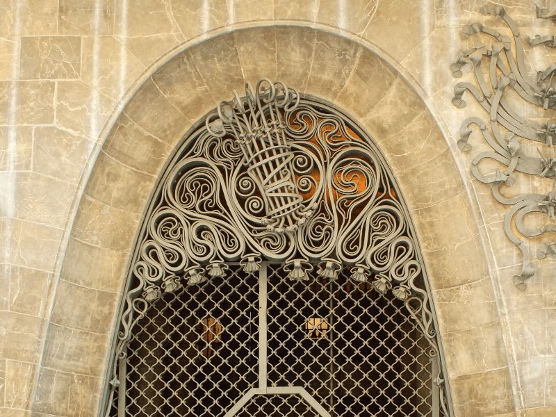 the taupe stone and ornate wrought-iron entryway of the Palau Guell building by gaudi in Barcelona