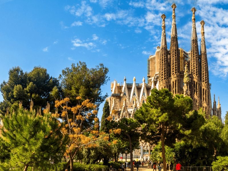 The exterior of the Sagrada Familia church with towers and beautiful plants in the gardens outside of the church in Barcelona on a sunny summer day at one of the most famous Gaudi buildings in Barcelona