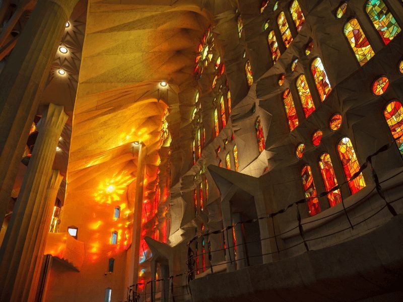 The interior colorful lights of Gaudi's Sagrada Familia Church with orange, yellow, reddish tones lighting up the church walls