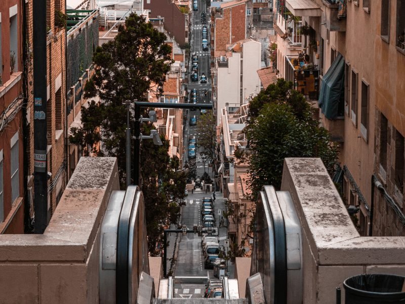 the elevator of baixada de gloria in Barcelona with very steep  hill cityscape below it, and an elevator with a small narrow opening here