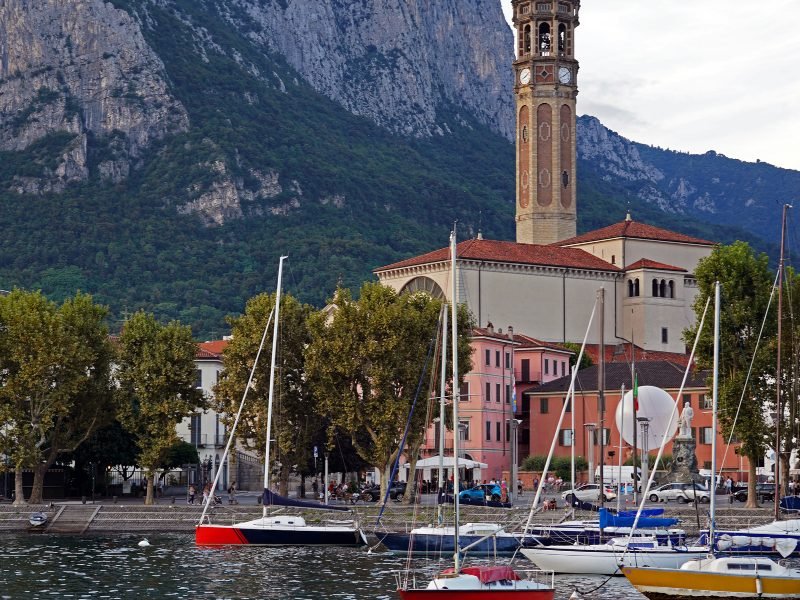 The town of Lecco with its harbor and church with clocktower and mountains behind it