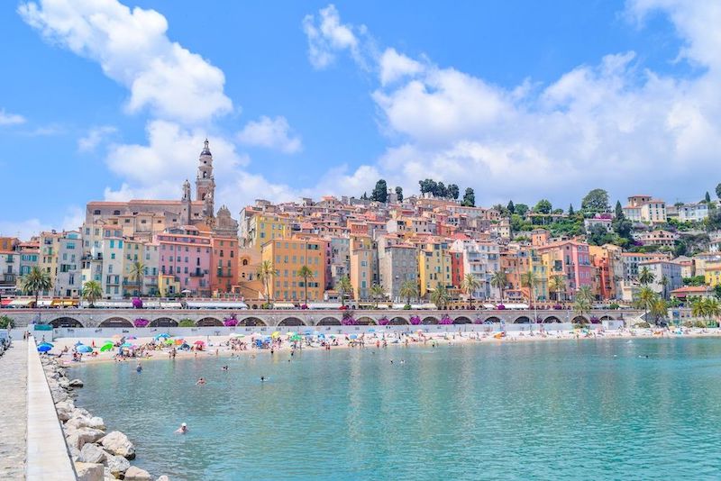 Colorful village of Menton, France with pastel buildings of every color in the rainbow as well as a public beach and church in the skyline