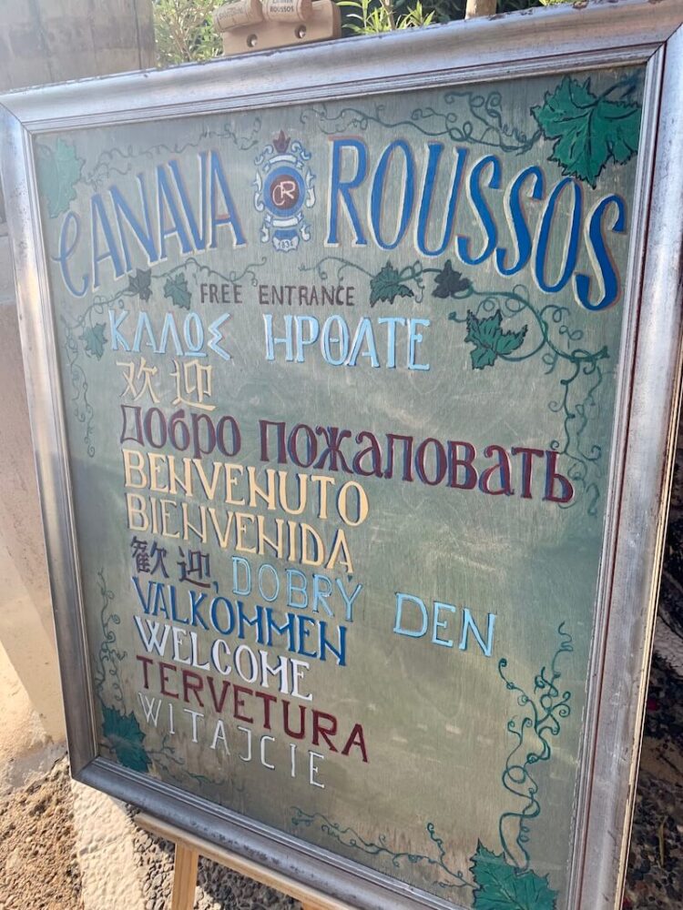 sign for roussos winery in santorini with welcome in many different languages