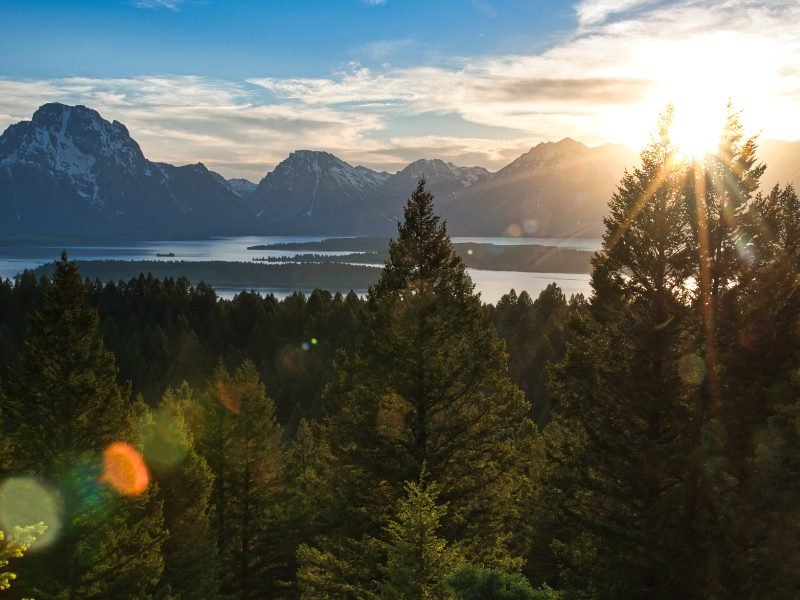 The views from Signal Mountain at sunset, with lake and waterways and mountains and trees, and sunburst from the sun sinking into the horizon