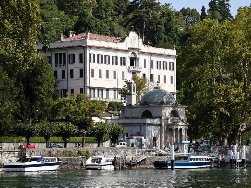 The villa carlotta on the lakefront with boats in front of it -- a beautiful white building with a dome-like structure in front of it and historic beautiful gardens