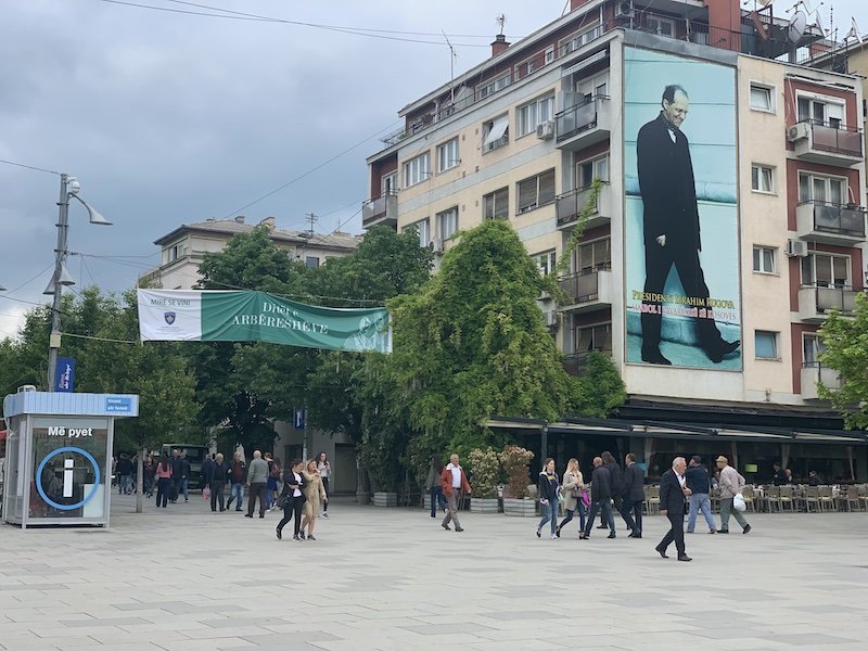 People walking around in Kosovo in a main square area with street signs and buildings