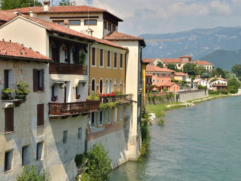 The charming town of Bassano del Grappa located on a river with white-washed buildings and historic architecture alongside the river.