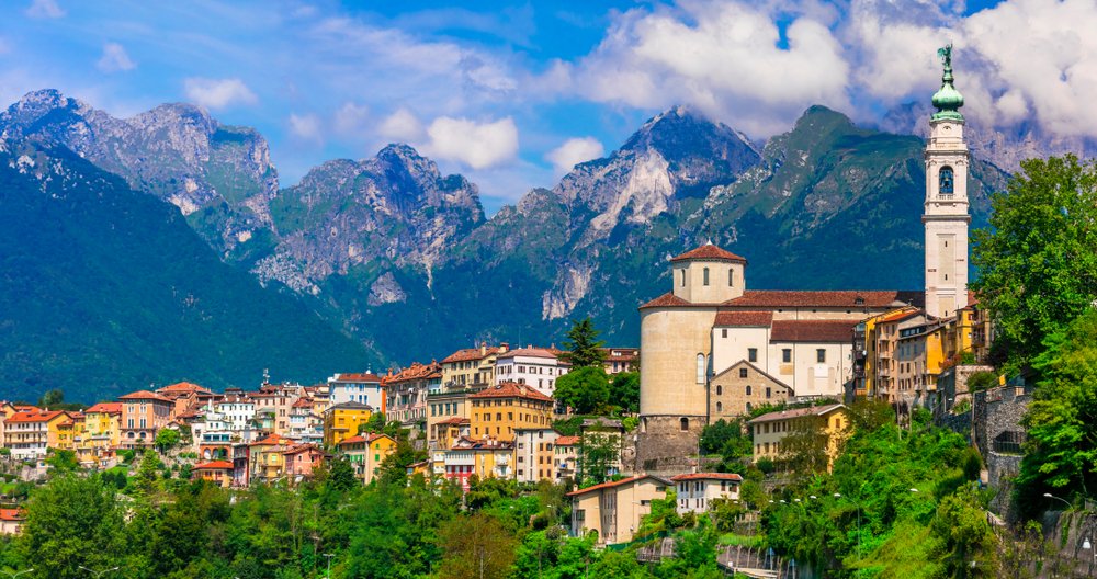 The village of Belluno with clocktower, Dolomite mountains, and colorful town, trees in the foreground