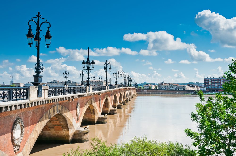 pinkish-taupe stones of the bridge of bordeaux with light fixtures and water in the river garonne on a sunny day in the city