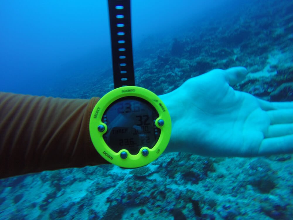 Yellow suunto dive computer on someone's hand underwater