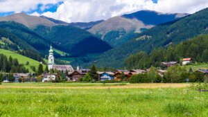 grassy meadow in front of the town of dobbiaco in the dolomites with rolling hills behind the town and partly cloudy sky