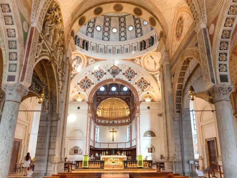 another view of the interior of the milan duomo, the nave, with arches, ornate detailing on the pillars and cupola, and stained glass elements