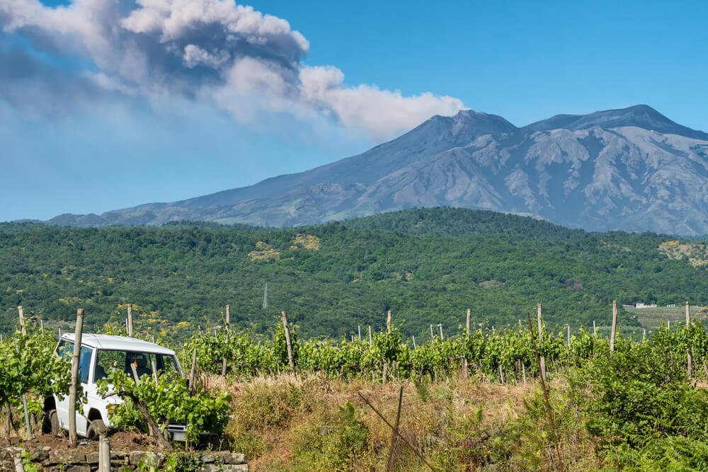 mt etna smoking in the background with vineyards in front and an agricultural tractor-type car in the front