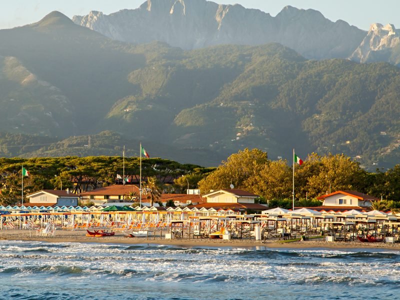 beach at forte dei marmi with italian flags on the beach, mountains in the background, and lido (beach club) umbrella and chairs