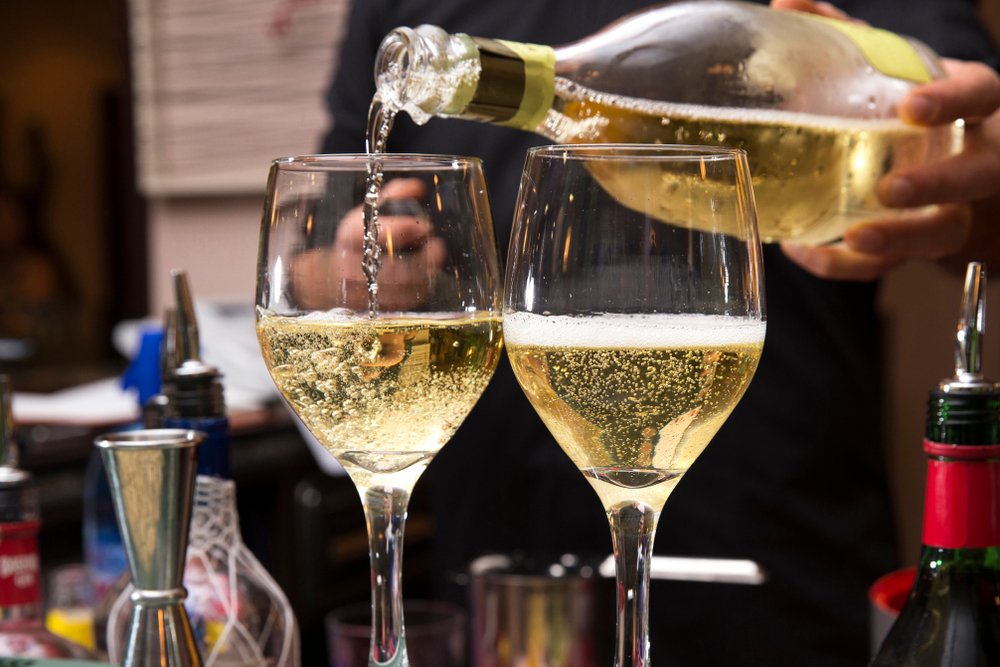 horizontal closeup of a barman pouring two glasses of franciacorta, italian wine, on the bar counter
