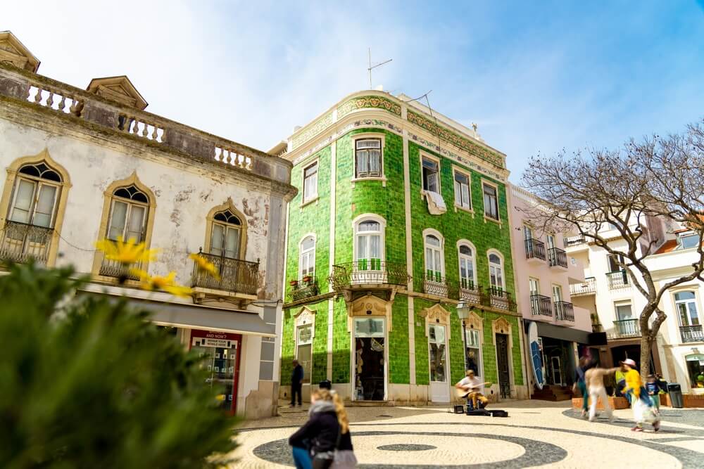 Historical town center in Lagos, Algarve, Portugal with moving people and a green tiled building in the city center area