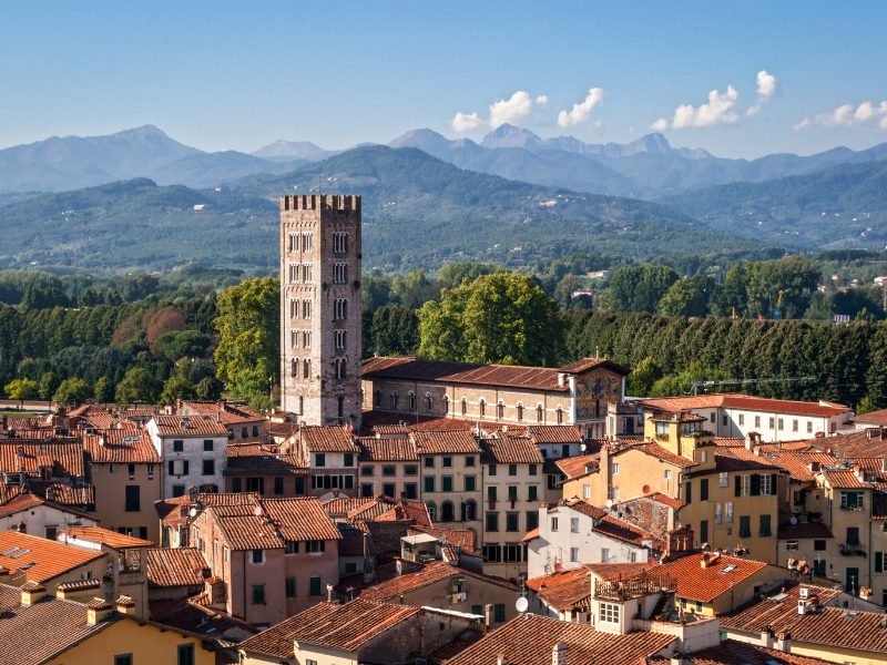 Large belltower or clocktower in Lucca, looming above the city's houses and skyline, with hills behind it showing the Tuscan countryside