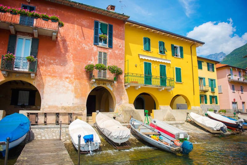 View of the dock and colorful buildings in shades of yellow, pink, and red, in Mandello del Lario on Italy's Lake Como.
