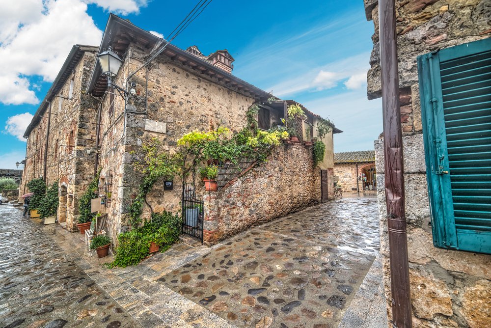 a town in monteriggioni with blue shutters, lots of plant life, stonework