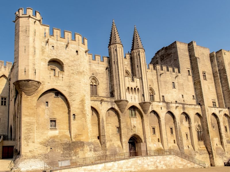 The front side of the papal palace with stone and lots of archways in the facade of the building and one small door