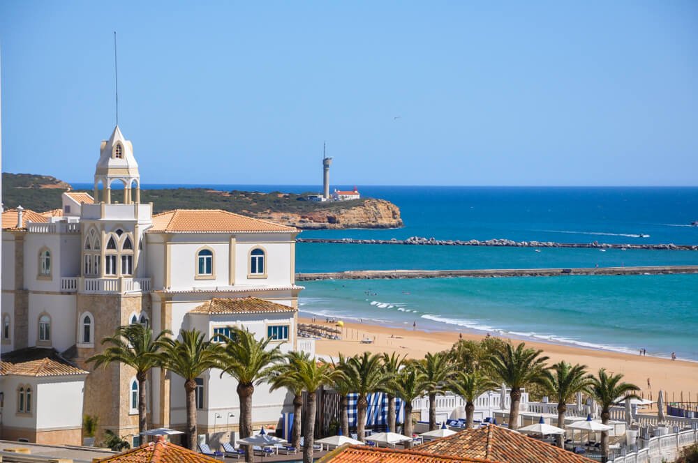 Beautiful Praia de Rocha in Portimao Portugal, along the coast with blue waters, soft white sand, a church, and a lighthouse in the distance