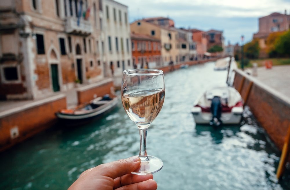 A glass of white wine overlooking a canal in Venice with boats