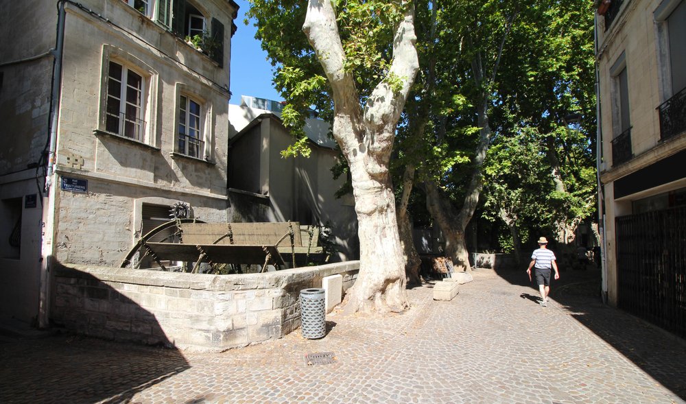 The famous rue tentiers with a water mill visible int eh canal and one person walking down the street in the summer wearing shorts and a hat
