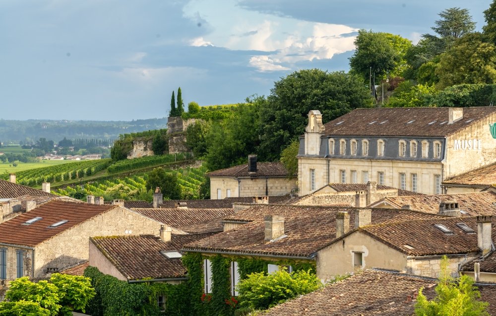 The old town of Saint-Emilion with views of rows of vineyards off in the distance on a mostly sunny day
