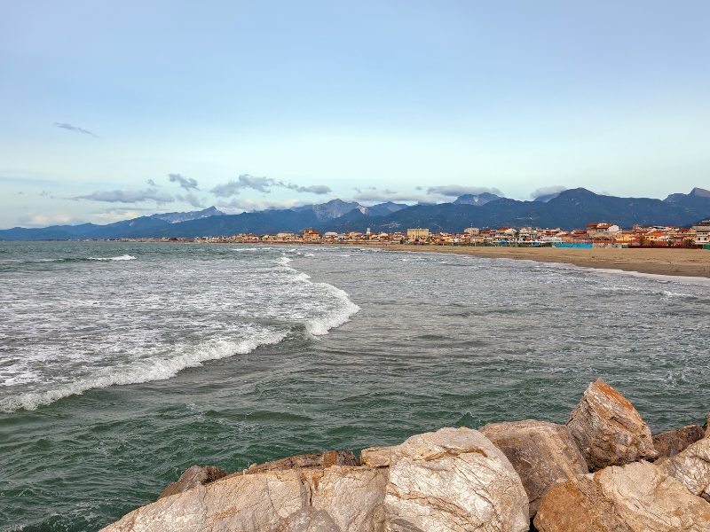 the beach front in viareggio, with sand, liberty-style architecture buildings, and mountains as the background