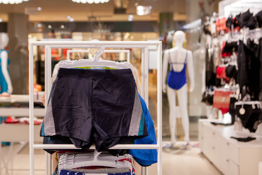 bathing suit section of a store with plain navy men's swim shorts with stripes on it