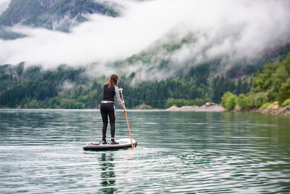 woman in a wetsuit paddleboarding on a lake with misty, cloudy weather