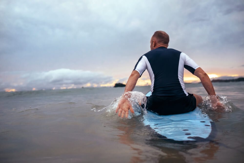 man in black and white rashguard sitting on a light blue surfboard