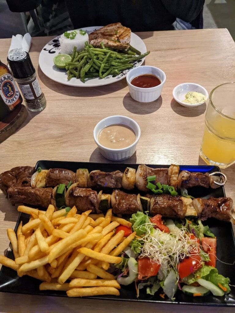 a plate of beef skewers with fries, salad, and cheese sauce