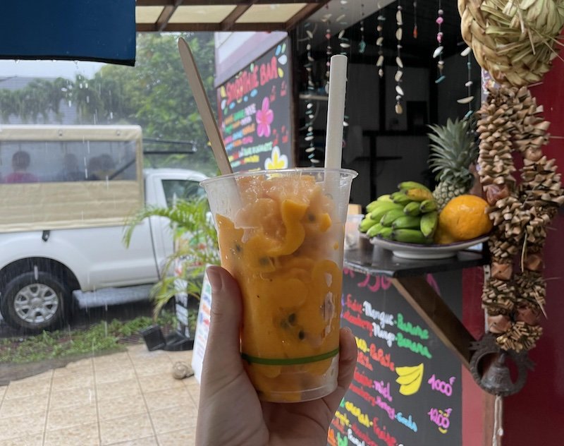 holding a passionfruit smoothie outside a smoothie stand in the rain