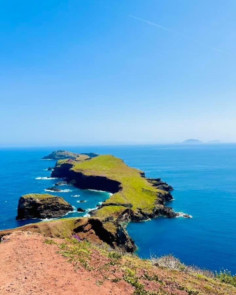 Rugged terrain of Ponta de Sao Lourenco nature reserve looking out on the Atlantic ocean with clear skies on a sunny day and other small islands in the distance on the horizon