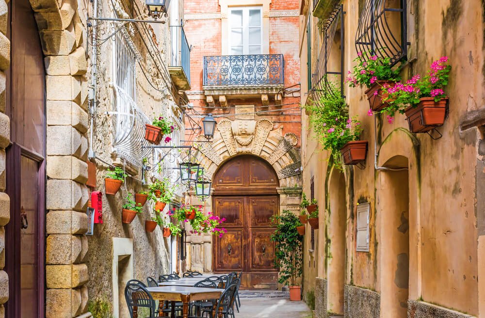 Cafe tables and chairs outside in old cozy street in the Positano town, with brick wall, flower pots with pink flowers, juliet balcony, windows